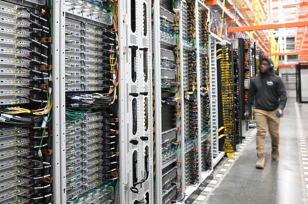 Network racks with high-density patch panels and colour-coded cabling, with an engineer walking the aisle